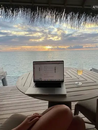 A laptop on a sunlit table overlooking the ocean at sunset